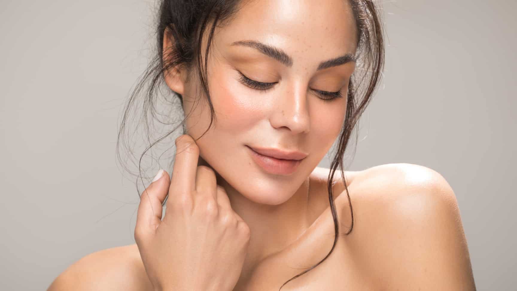 Model with glowing skin touching her neck, eyes closed