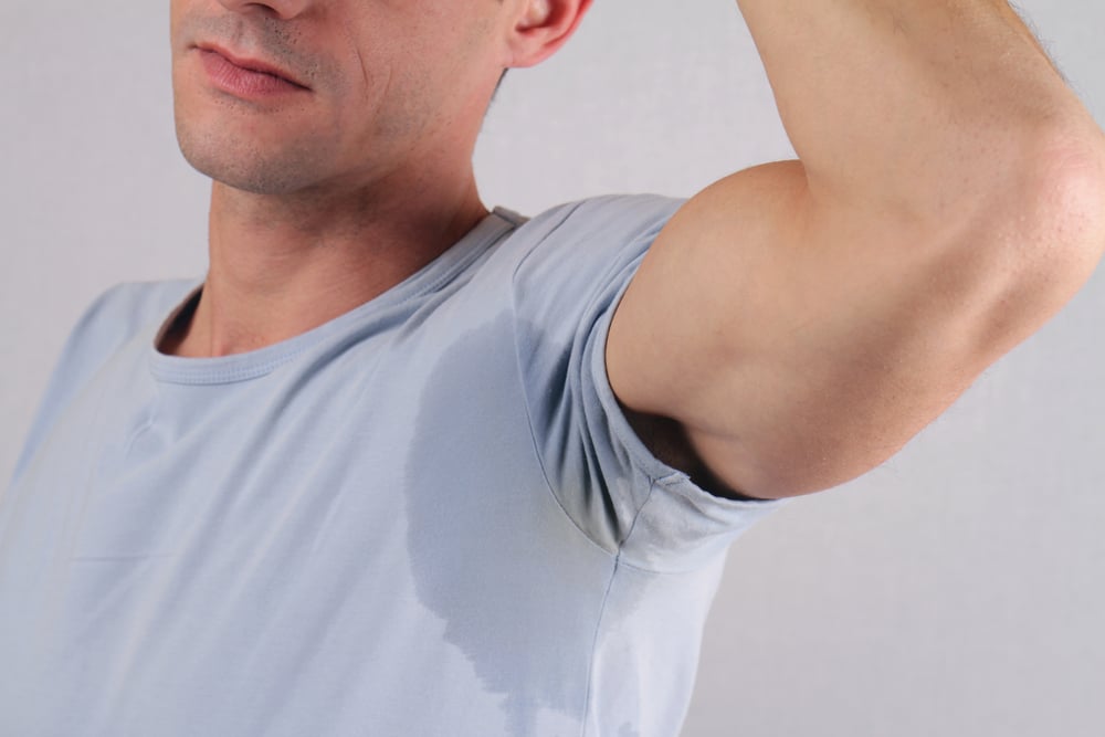 Model raising his arm, a sweat mark on the underarm of his T-shirt