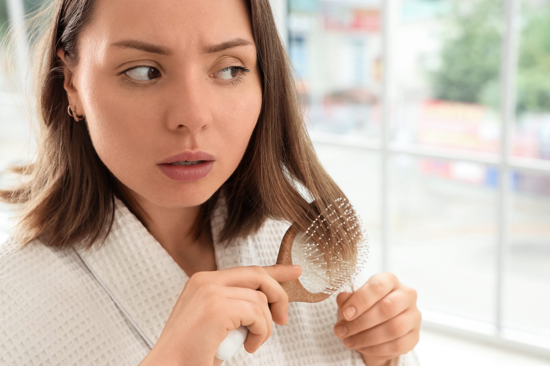 Model looking worriedly at a hairbrush full of fallen hair