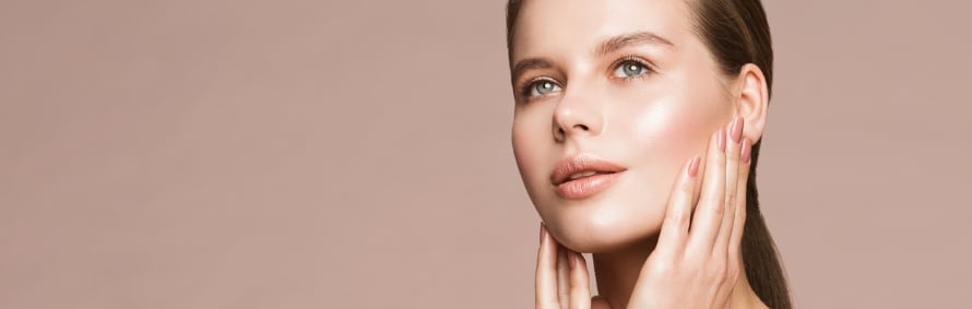 Model with dewy skin, fingertips on her cheek, on a warm beige background