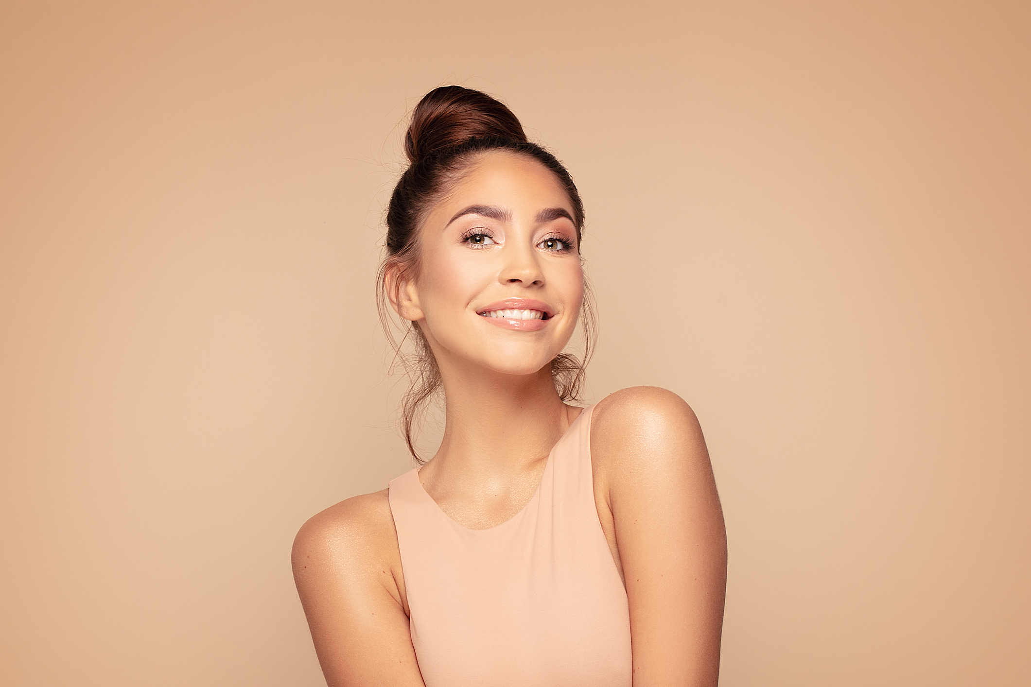 Smiling model with her hair in a bun, on a peach background