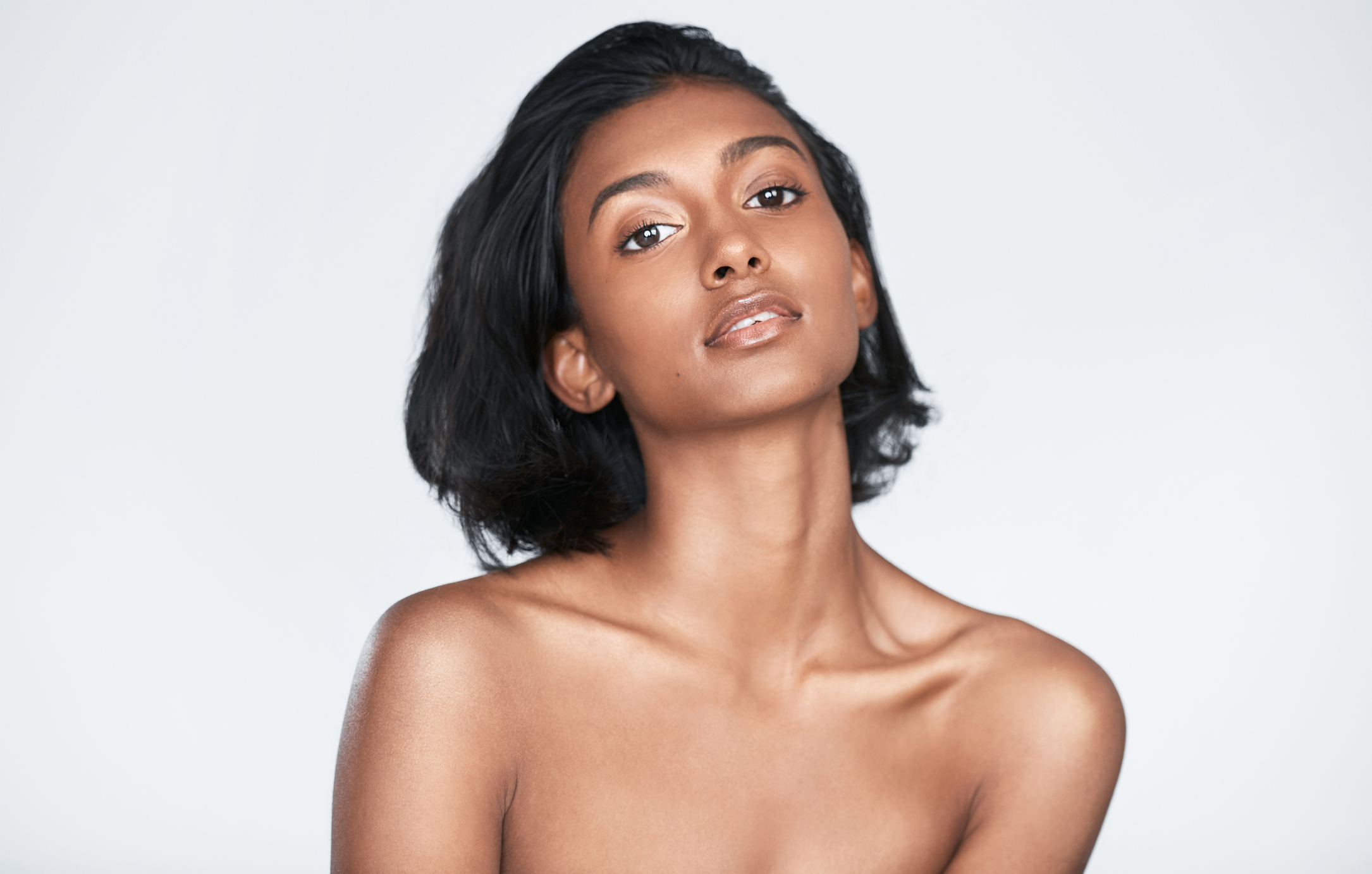 Model with short dark hair and bare shoulders, on a white background