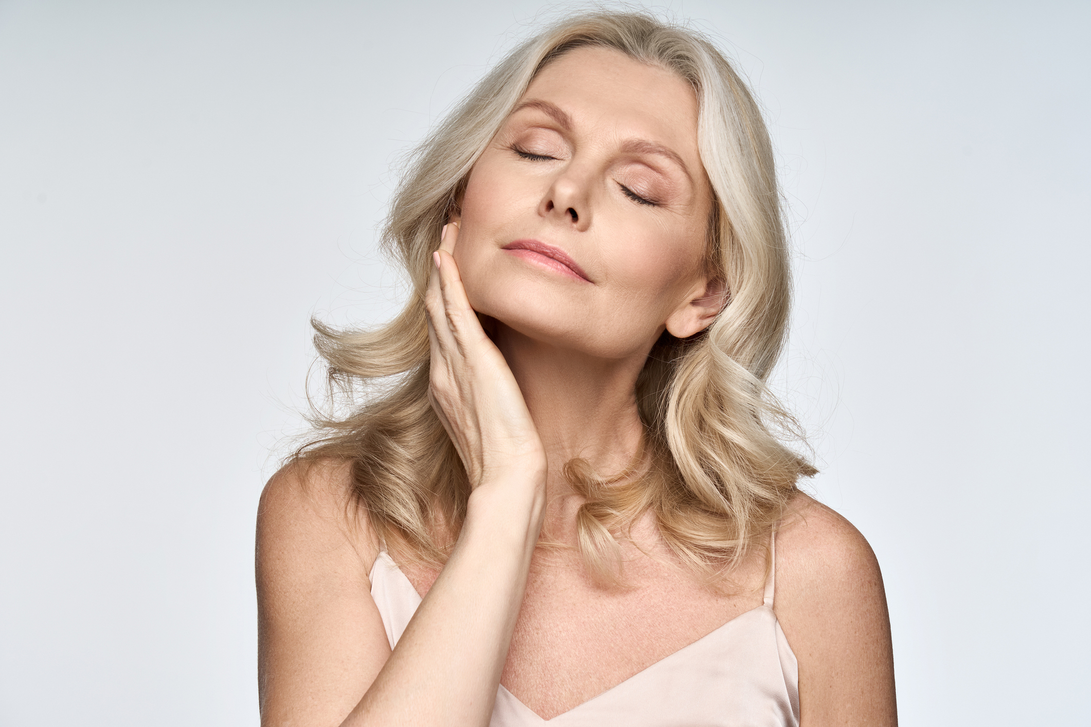 Mature model with wavy blonde hair, eyes closed, hands at her face