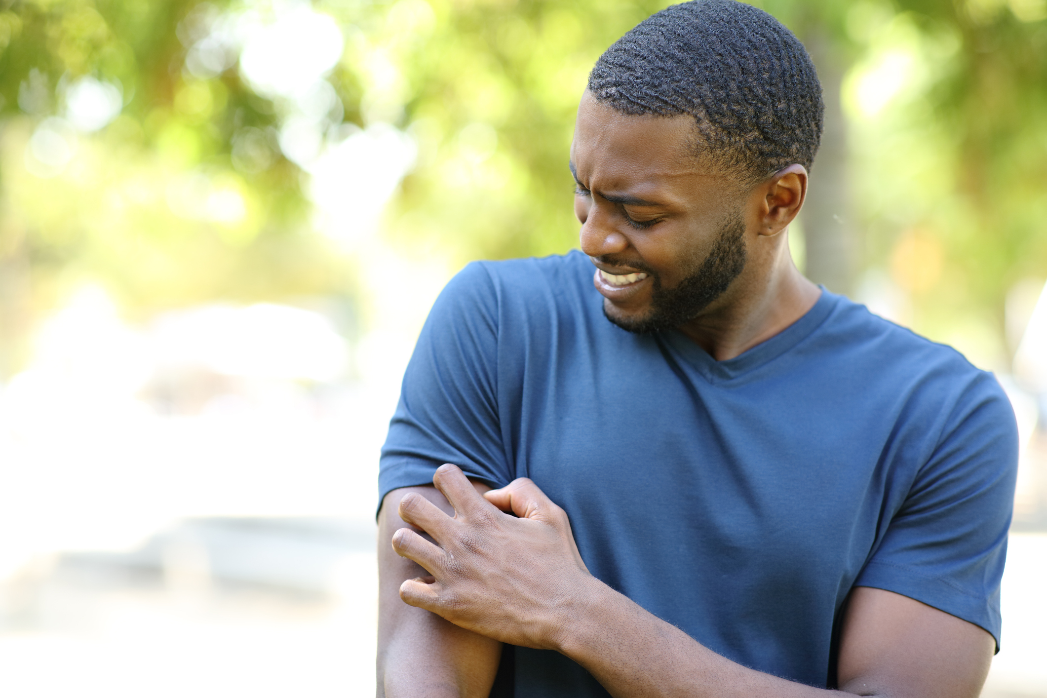 Man in a blue T-shirt looking at an itchy patch on his arm