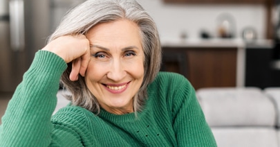 Smiling senior model with grey hair, chin on her hand, in a green sweater