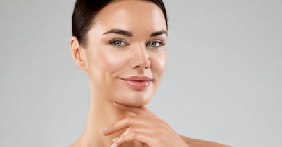 Model with her hair pulled back touching her jaw, on a grey background