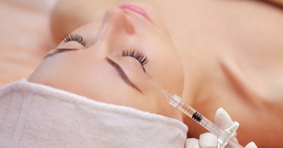 Model reclining with eyes closed as a fine needle approaches her cheek
