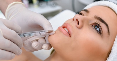 Gloved clinician injecting filler near a model's lips