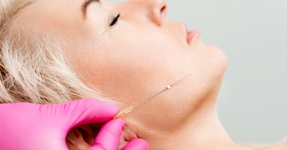 Model reclining as a gloved hand places a thread at her jawline