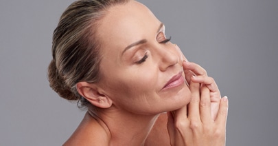 Mature model with her hair up, hands at her cheeks, eyes closed