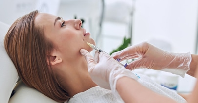 Model reclining as a clinician injects filler near her mouth