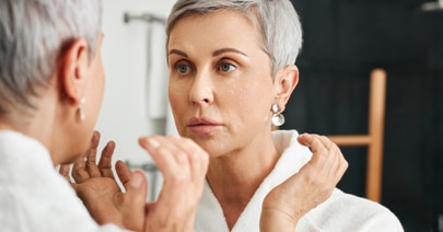 Two mature women face to face, one touching her cheek in a mirror