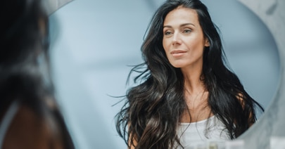 Model with long dark wavy hair in a round mirror frame