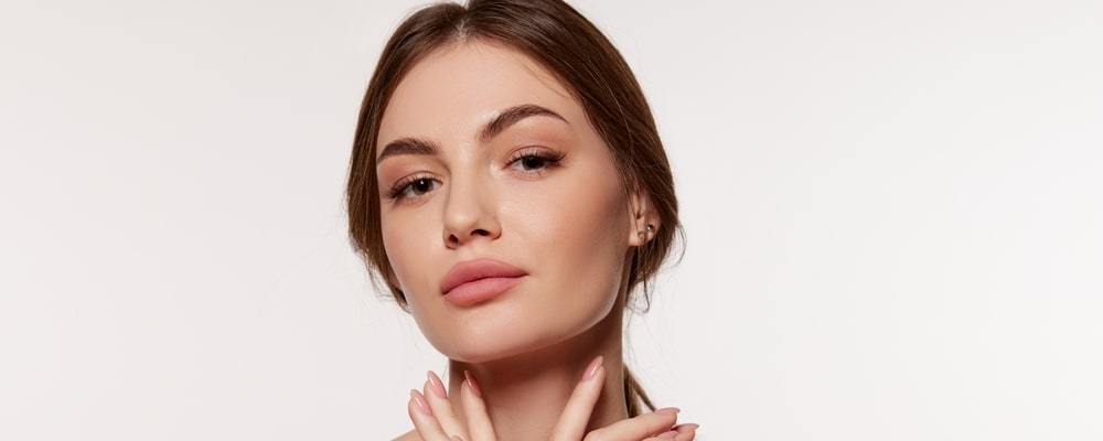 Model with smooth skin and dark hair pulled back, one hand at her neck, on a light background