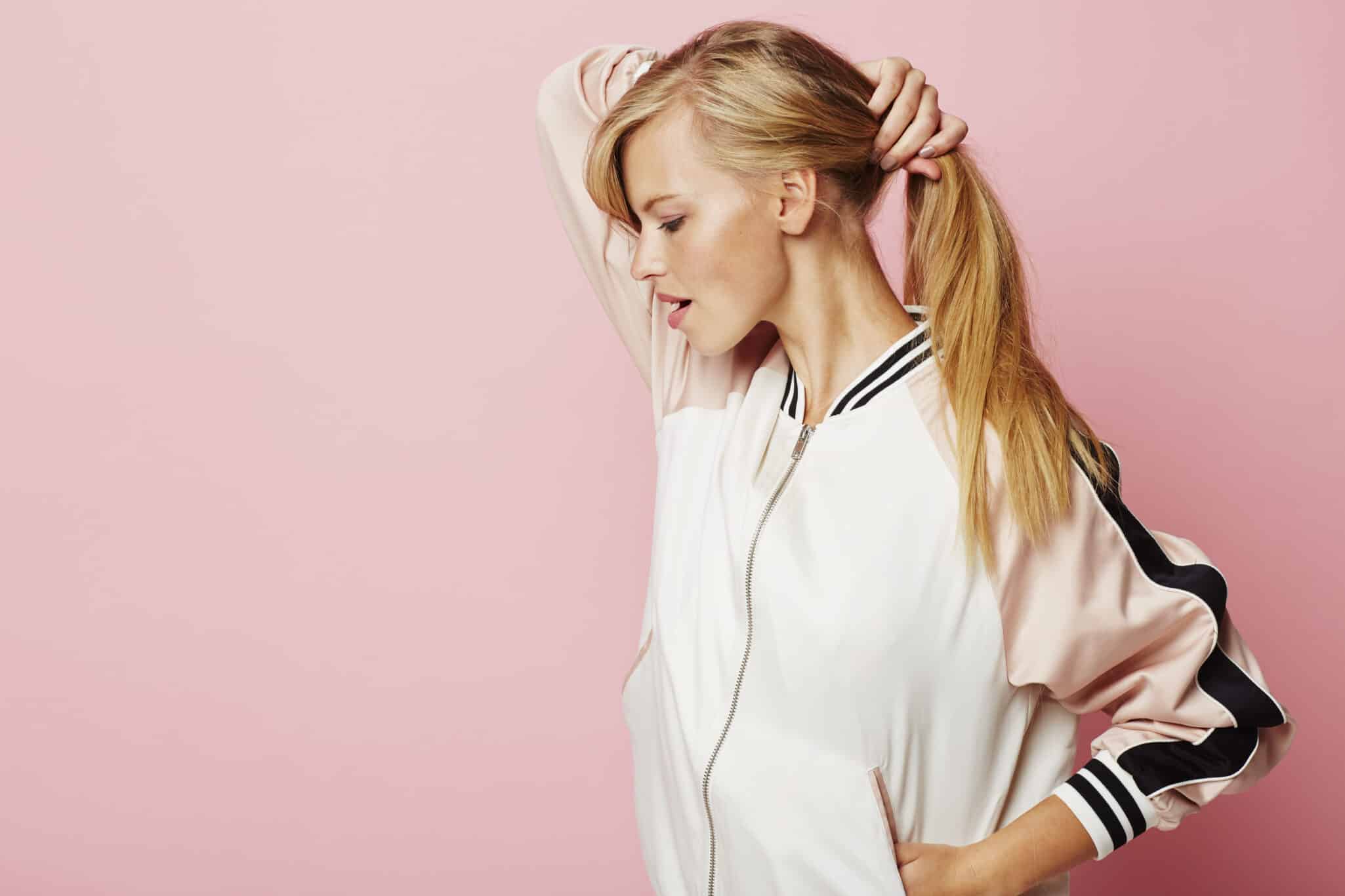 Blonde woman holding her ponytail loosely to ease tension and prevent hair loss