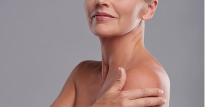 Mature model's jawline and neck, a hand at her collarbone, on a grey background