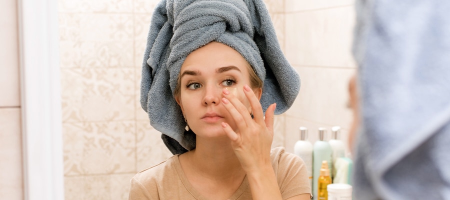 A beautiful girl with a towel on her head sticks hydrogel patches under her eyes on her face. The girl cares for the skin and moisturizes the area around the eyes. Home care treatments in the bathroom