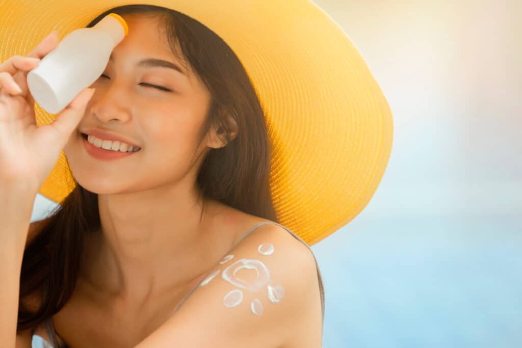 Attractive woman with healthy skin applying sunscreen on a sunny day and holding holding blank sunscreen UV protective lotion bottle