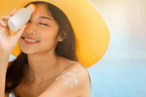 Attractive woman with healthy skin applying sunscreen on a sunny day and holding holding blank sunscreen UV protective lotion bottle