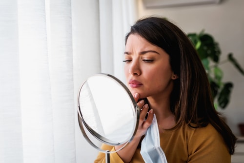 Woman looking herself in the mirror concerned about acne, maskne
