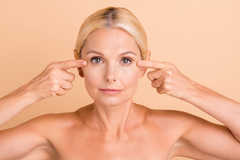 Beautiful older woman pointing at her eyes to show the difference Upneeq subtle eyelid lifting drops have made. Beautiful older woman pointing at her eyes to show the difference Upneeq subtle eyelid lifting drops have made.