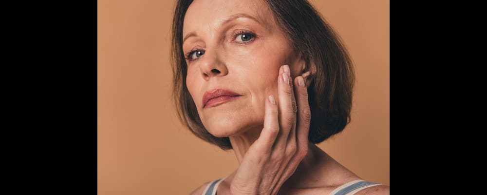 Older woman touching her face after receiving professional skincare treatments and recommendations.