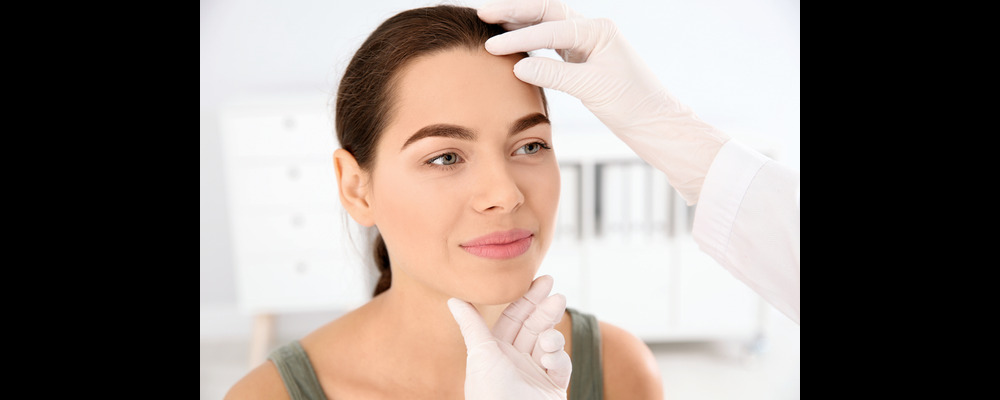 Woman smiling while having a routine dermatology exam done as an act of self-care.