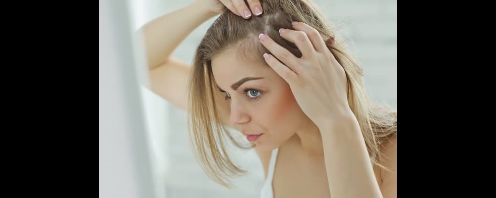 Beautiful woman checking her scalp in the mirror after suffering from accelerated hair loss.
