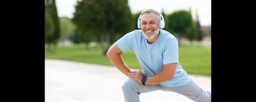 Smiling man with headphones on, stretching before his run and in need of skincare tips to protect himself.