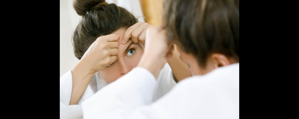 Close-up of a young woman looking at the hormonal acne breaking out on her forehead.